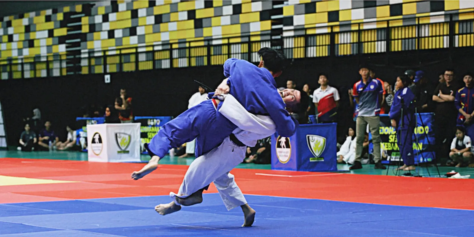 A judoka in blue throws an opponent at a tournament